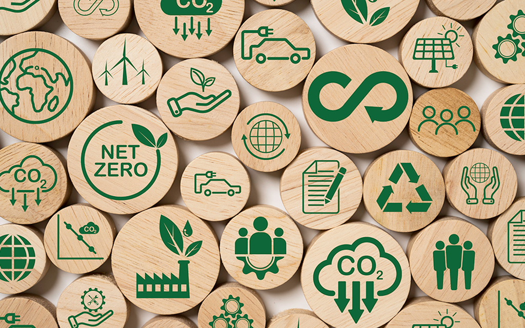 Wooden blocks with green sustainability icons including net zero, CO2 reduction, renewable energy, recycling, and circular economy.